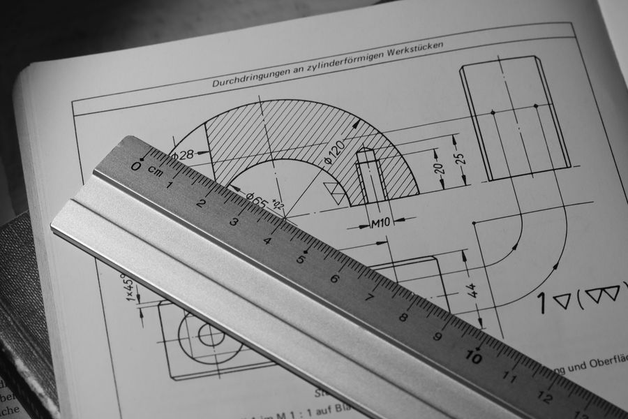 An engineering drawing of a machined part with a steel ruler laid across it